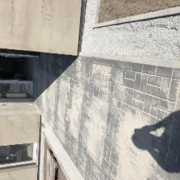 Widok z góry na nowo ułożoną, szarą kostkę brukową w geometryczny wzór, obok świeżo przygotowany teren pod trawnik z drobnym żwirem, cień osoby fotografującej.