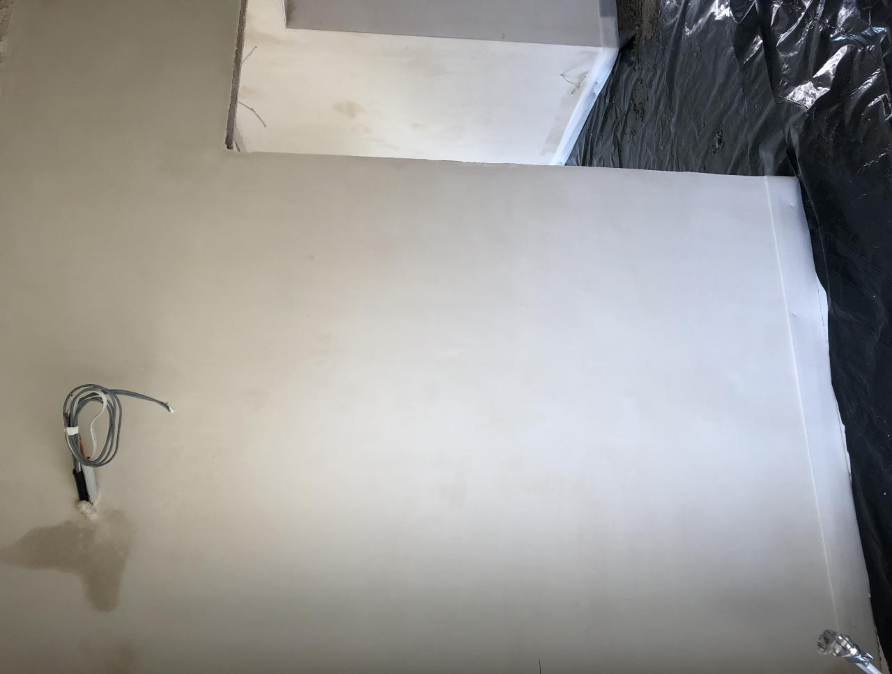 Świeżo położone, gładkie tynki na ścianach w pomieszczeniu w trakcie remontu, widoczne kable wystające ze ściany i folia ochronna na podłodze.