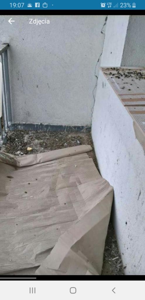 Balkon przed sprzątaniem: zabrudzona podłoga z resztkami gruzu i zabezpieczona kartonem, widoczne pęknięcie na ścianie.