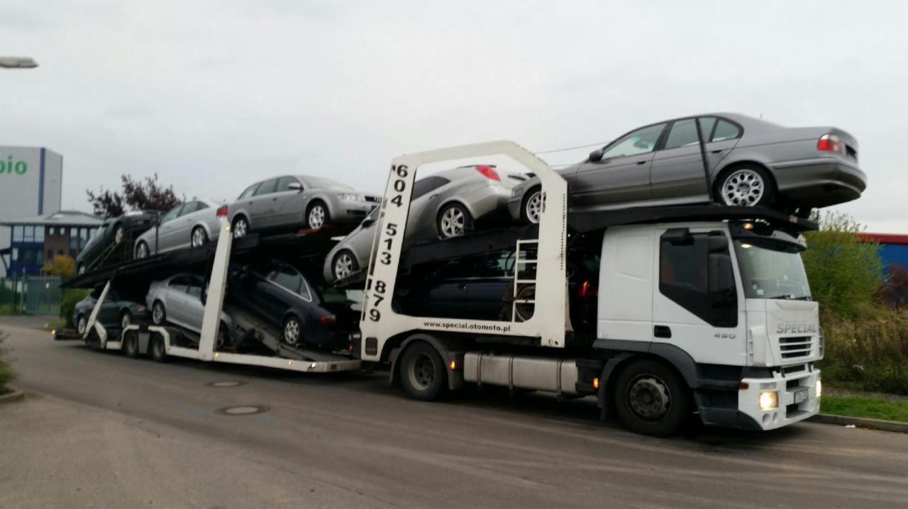 Ciężarówka z lawetą przewozi kilka samochodów osobowych na dwupoziomowej platformie transportowej.