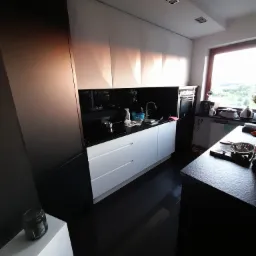 Nowoczesna kuchnia z białymi szafkami i czarnym blatem, oświetlona światłem dziennym wpadającym przez okno. Minimalistyczny design i czyste linie.