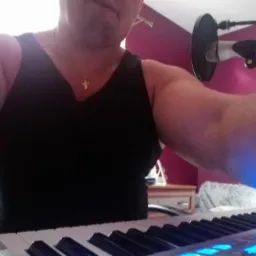 Mężczyzna w czarnym podkoszulku gra na keyboardzie, mikrofon na statywie w tle, ujęcie z bliska.