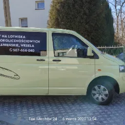 Jasnożółty bus z grafiką samolotu i napisem 'Transfery na lotniska, obsługa przyjęć okolicznościowych'. Numery telefonów widoczne na pojeździe.