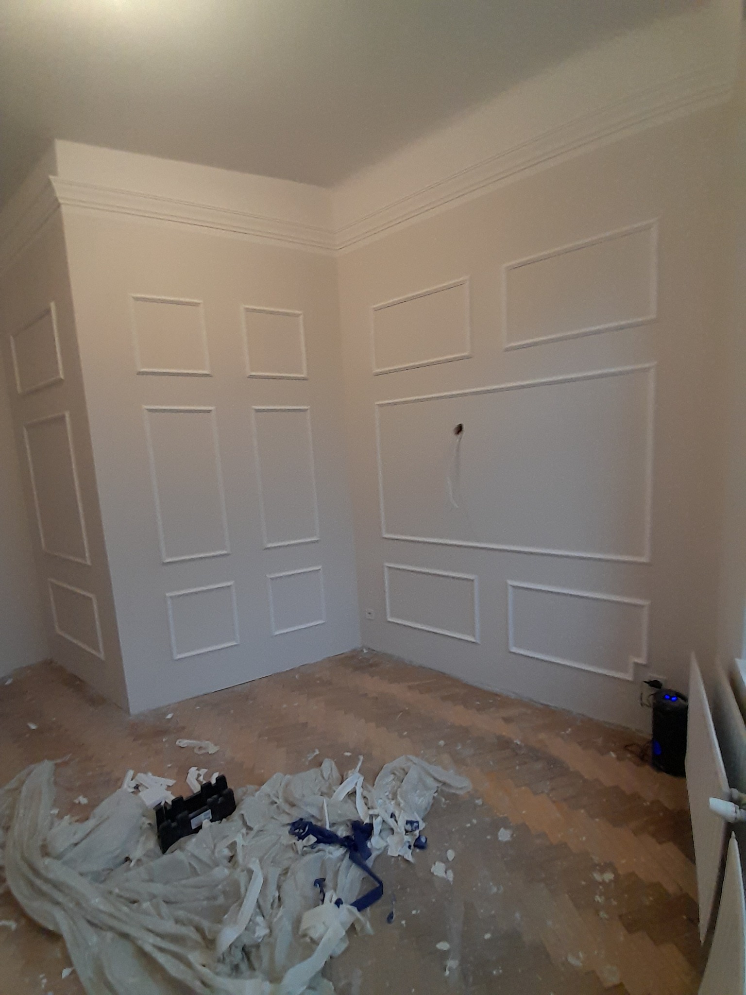 Pokój z zamontowanymi sztukateriami ściennymi w formie paneli z listew, widoczne ślady po pracach na podłodze.