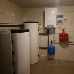 W.H GROUP Sp. z o.o. - Kompletna instalacja grzewcza w kotłowni: biały piec gazowy De Dietrich, dwa białe i jeden szary zbiornik akumulacyjny, czerwony i niebieski zbiornik przeponowy.