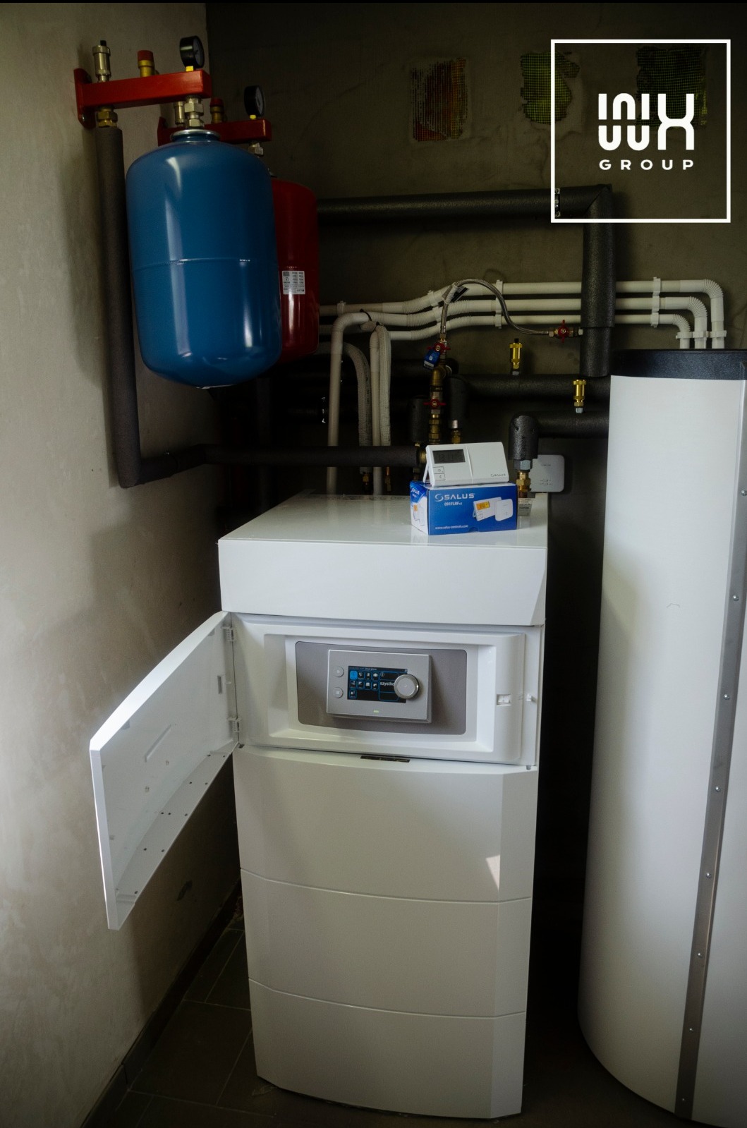 Nowoczesny, biały piec gazowy z otwartymi drzwiczkami i dotykowym panelem sterowania, obok zasobnik ciepłej wody. Instalacja grzewcza w tle.