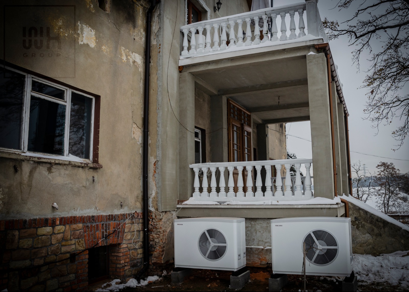 Dwie pompy ciepła Stiebel Eltron na zewnątrz budynku z balkonem i balustradami. Widoczny fragment elewacji z oknem i ceglaną podmurówką.