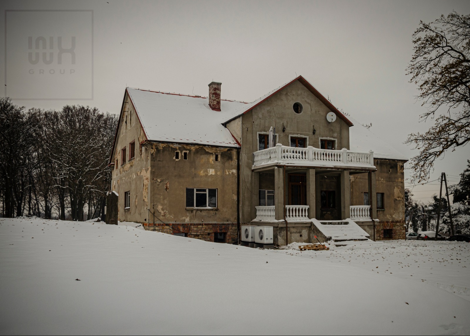 Dwukondygnacyjny, zaniedbany dom z balkonem, pokryty śniegiem. Widoczne ślady odpadającego tynku i dwa klimatyzatory na zewnątrz. Na dachu śnieg. Pochmurne niebo.