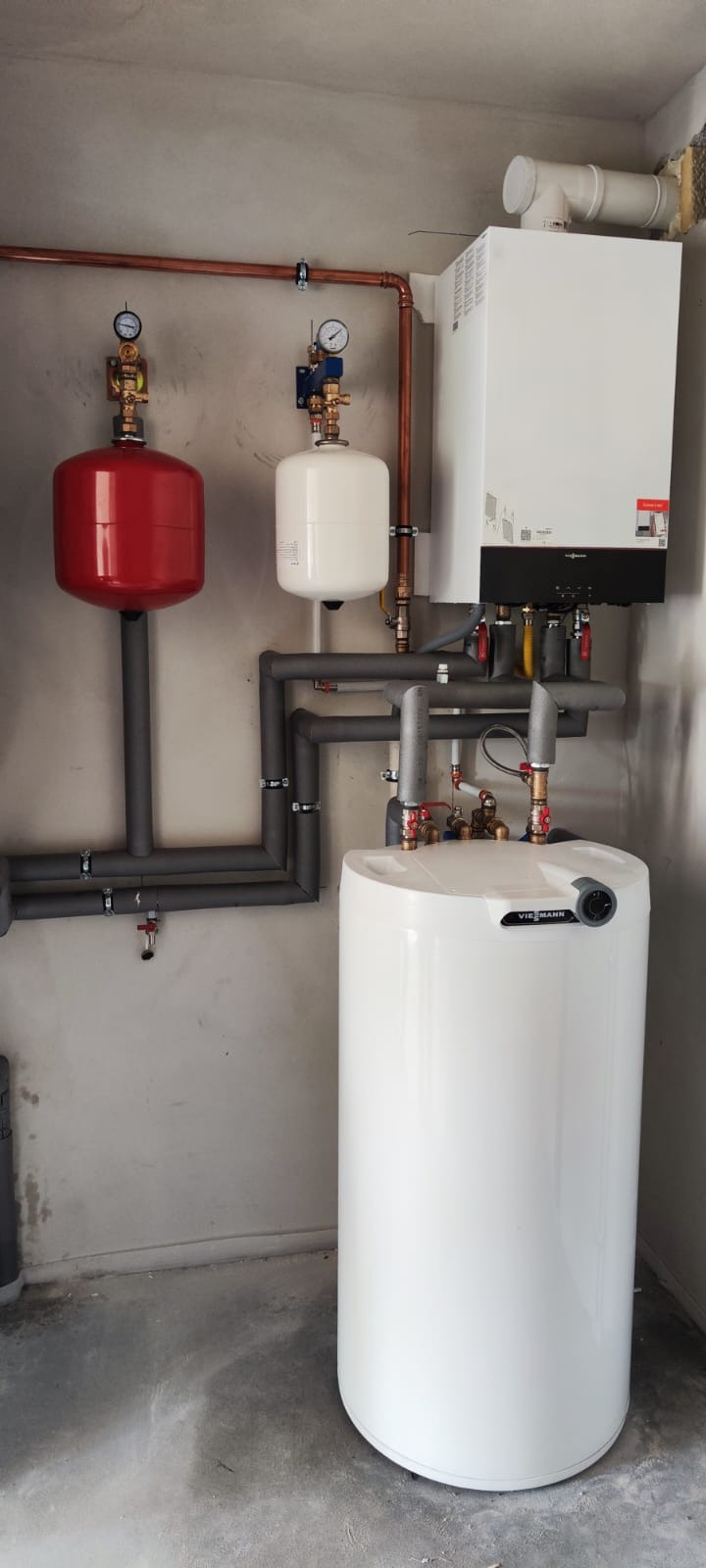 Zamontowany kocioł Viessmann z zbiornikiem i instalacją w kotłowni w Krakowie. Widoczne rury miedziane i szare izolowane, manometry. Nowoczesna instalacja grzewcza.