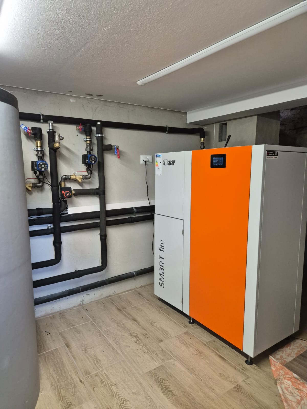 Zamontowany piec na paliwo stałe marki Lazar Smart Fire z podłączoną instalacją CO w kotłowni z wykończonymi ścianami i podłogą.