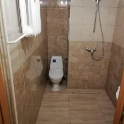 Ukończona łazienka z brązowymi płytkami imitującymi marmur, białą toaletą i grzejnikiem drabinkowym.