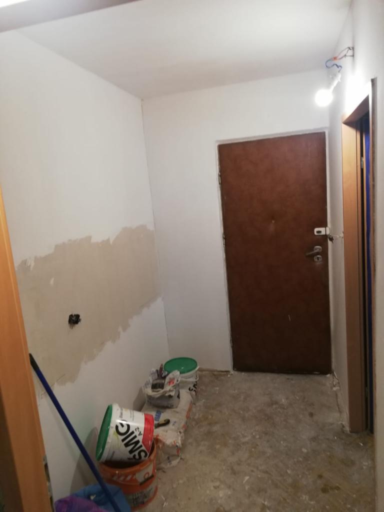 Wnętrze w Gnieźnie w trakcie prac przygotowawczych do malowania: ściana z częściowo zaszpachlowanymi ubytkami, widoczne puszki z farbą i narzędzia malarskie.