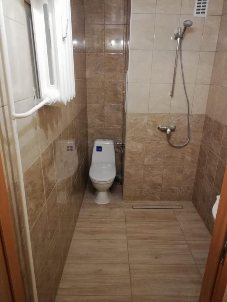 Ukończona łazienka z brązowymi płytkami imitującymi marmur, białą toaletą i grzejnikiem drabinkowym.