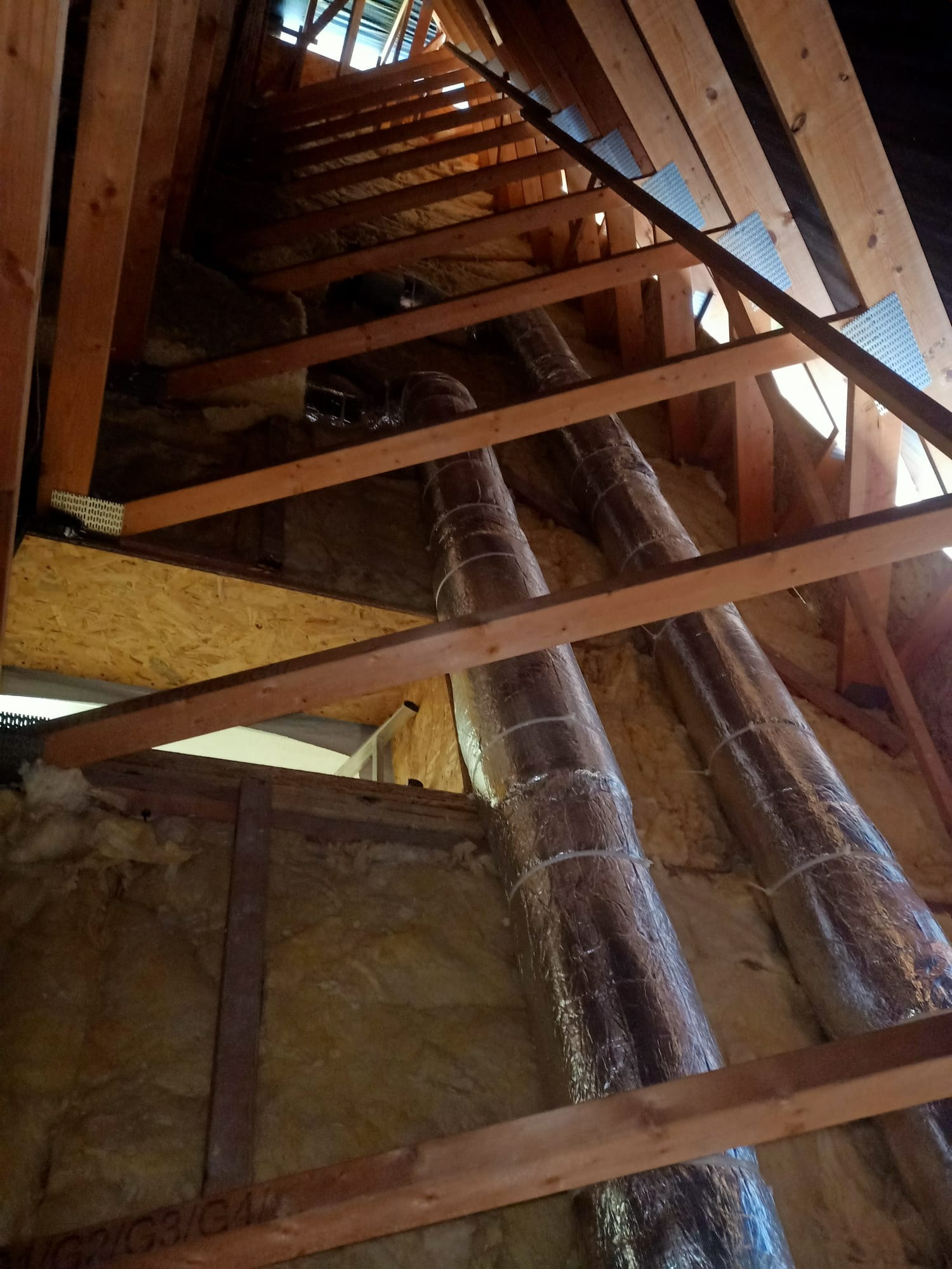 Dwie rury wentylacyjne w izolacji, zamontowane pod skośnym dachem poddasza w Gorzowie Wielkopolskim, widoczne drewniane elementy konstrukcyjne.