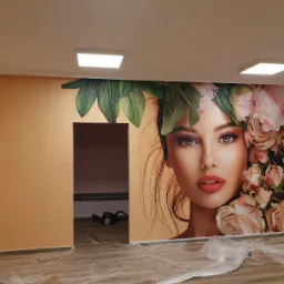 Fototapeta z wizerunkiem kobiety w kwiatach na ścianie w pokoju, zabezpieczona folią podłoga, widoczne oświetlenie sufitowe.