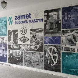 TOPAGO GROUP SPÓŁKA Z OGRANICZONĄ ODPOWIEDZIALNOŚCIĄ - Ściana z fototapetą prezentującą kolaż zdjęć maszyn i logo firmy ZAMET, z przewagą kolorów szarości i błękitu, w jasnym pomieszczeniu z oknem.