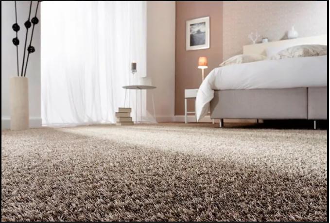 Beżowy dywan shaggy w sypialni z łóżkiem, stolikiem nocnym, lampką i zasłonami.