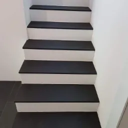 Schody wyłożone ciemną płytką, białe podstopnice, widok z dołu, szare płytki podłogowe