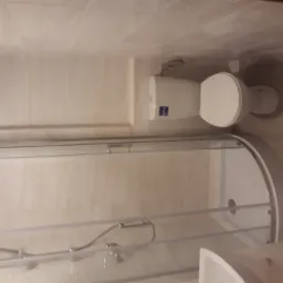 Biała toaleta i kabina prysznicowa z zaokrąglonymi drzwiami w wyłożonej płytkami łazience.