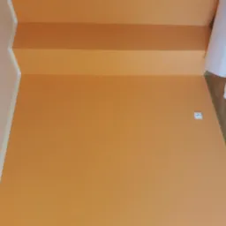 Pomarańczowe ściany i schody po malowaniu, widoczna rolka folii malarskiej przy ścianie i gniazdko elektryczne.