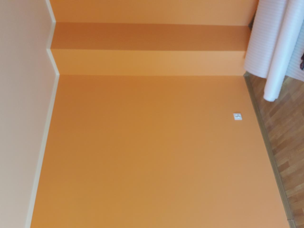 Pomarańczowe ściany i schody po malowaniu, widoczna rolka folii malarskiej przy ścianie i gniazdko elektryczne.