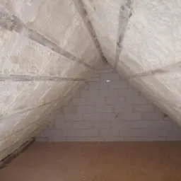 Poddasze po natrysku pianki izolacyjnej, widoczne drewniane krokwie i biała ściana z bloczków, podłoga wyłożona płytą OSB.