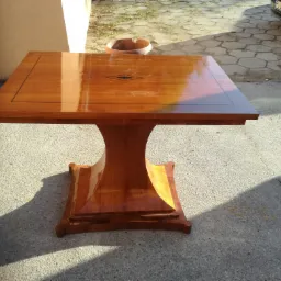 Lakierowany stół drewniany z intarsją w kształcie rombu na blacie, stojący na zewnątrz na betonowym podłożu, z fragmentem samochodu w tle.