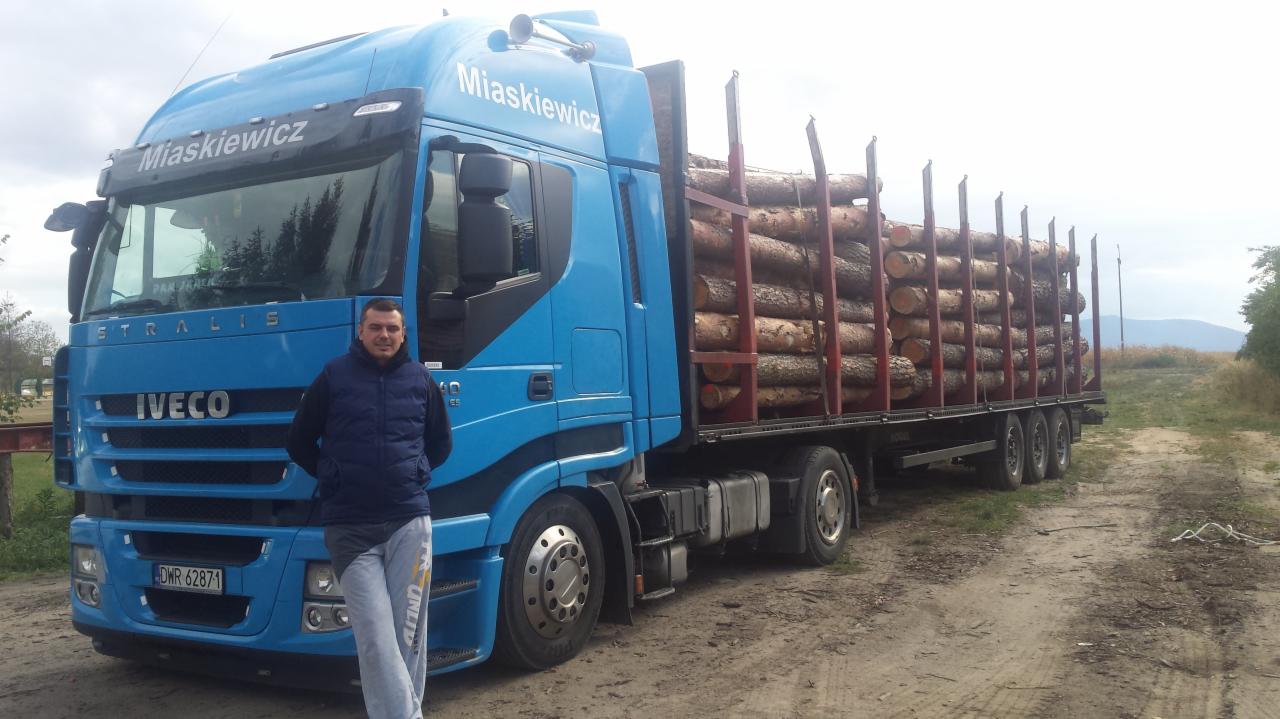 Niebieski samochód ciężarowy marki Iveco z nazwą firmy 'Miaskiewicz' przewożący drewno, zaparkowany w Czerńczycach na polnej drodze, z pracownikiem firmy stojącym przed pojazdem.