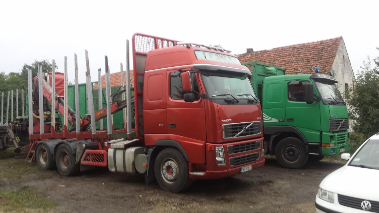 Czerwony i zielony samochód ciężarowy Volvo na błotnistym terenie, z urządzeniem do załadunku drewna na jednym z nich.
