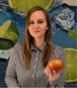 Kobieta w koszuli w paski trzymająca pomarańczowe jabłko na tle grafiki z limonkami i wodą.