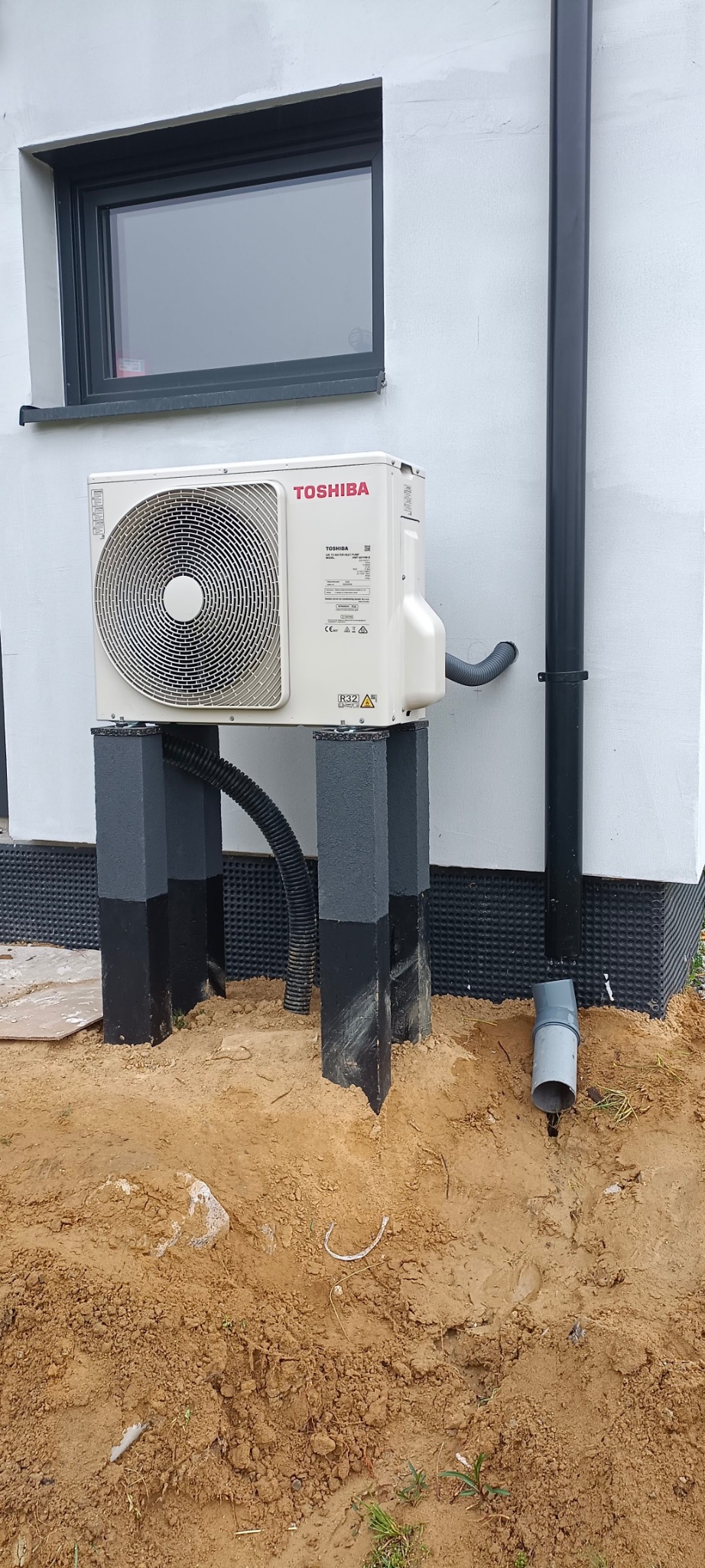 Zewnętrzna jednostka klimatyzacji Toshiba zamontowana na betonowych postumentach przy ścianie budynku w Jaworsku, widoczna instalacja odprowadzająca skropliny.