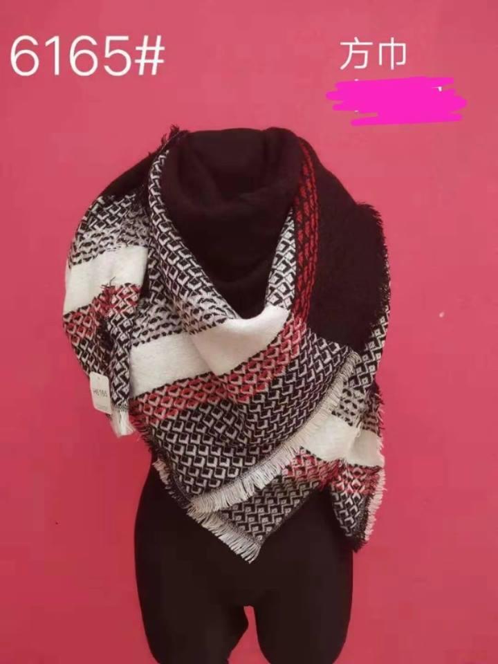 Manekin z dużym, kwadratowym szalem w geometryczny wzór: białe, czarne i czerwone romby, wykończony frędzlami, na różowym tle.