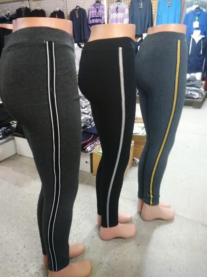 Trzy pary legginsów sportowych na manekinach: grafitowe z białymi paskami, czarne ze srebrnymi paskami i szare ze złotymi paskami, eksponowane w sklepie odzieżowym.