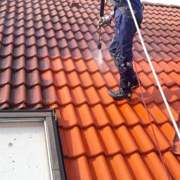 Błysk Paweł Szczepaniak - Pracownik w Ostrowcu Świętokrzyskim czyści czerwoną dachówkę za pomocą myjki ciśnieniowej, widoczna różnica między umytą a zabrudzoną częścią dachu.