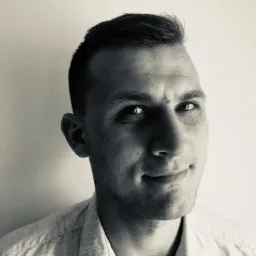 Portret mężczyzny w koszuli, w czerni i bieli, z subtelnym uśmiechem. Widoczne delikatne zmarszczki mimiczne.