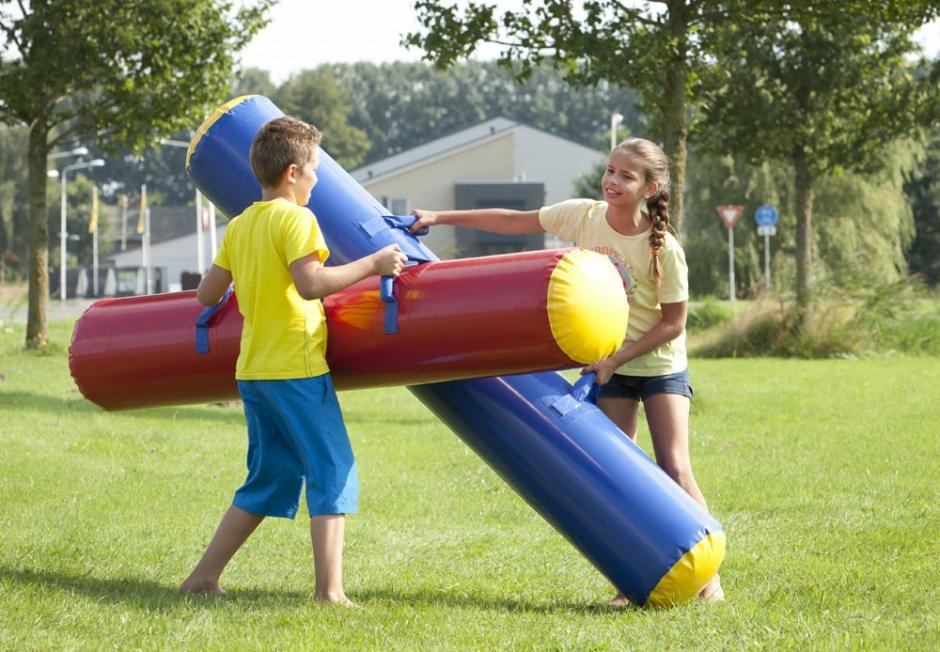 Dwoje dzieci, chłopiec i dziewczynka, bawi się na trawie z dużymi, kolorowymi dmuchanymi walcami połączonymi ze sobą.