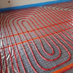 Ekover- Piotr Drabjewski - Czerwone rury ogrzewania podłogowego rozłożone na folii z siatką, zamocowane plastikowymi klipsami, widok z góry, przygotowane do wylania posadzki.