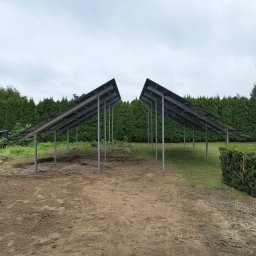 Ekover- Piotr Drabjewski - Montaż konstrukcji pod panele fotowoltaiczne na działce z zielenią. Widoczne metalowe słupki i częściowo zamontowane panele. Prace w toku, przygotowanie do instalacji.
