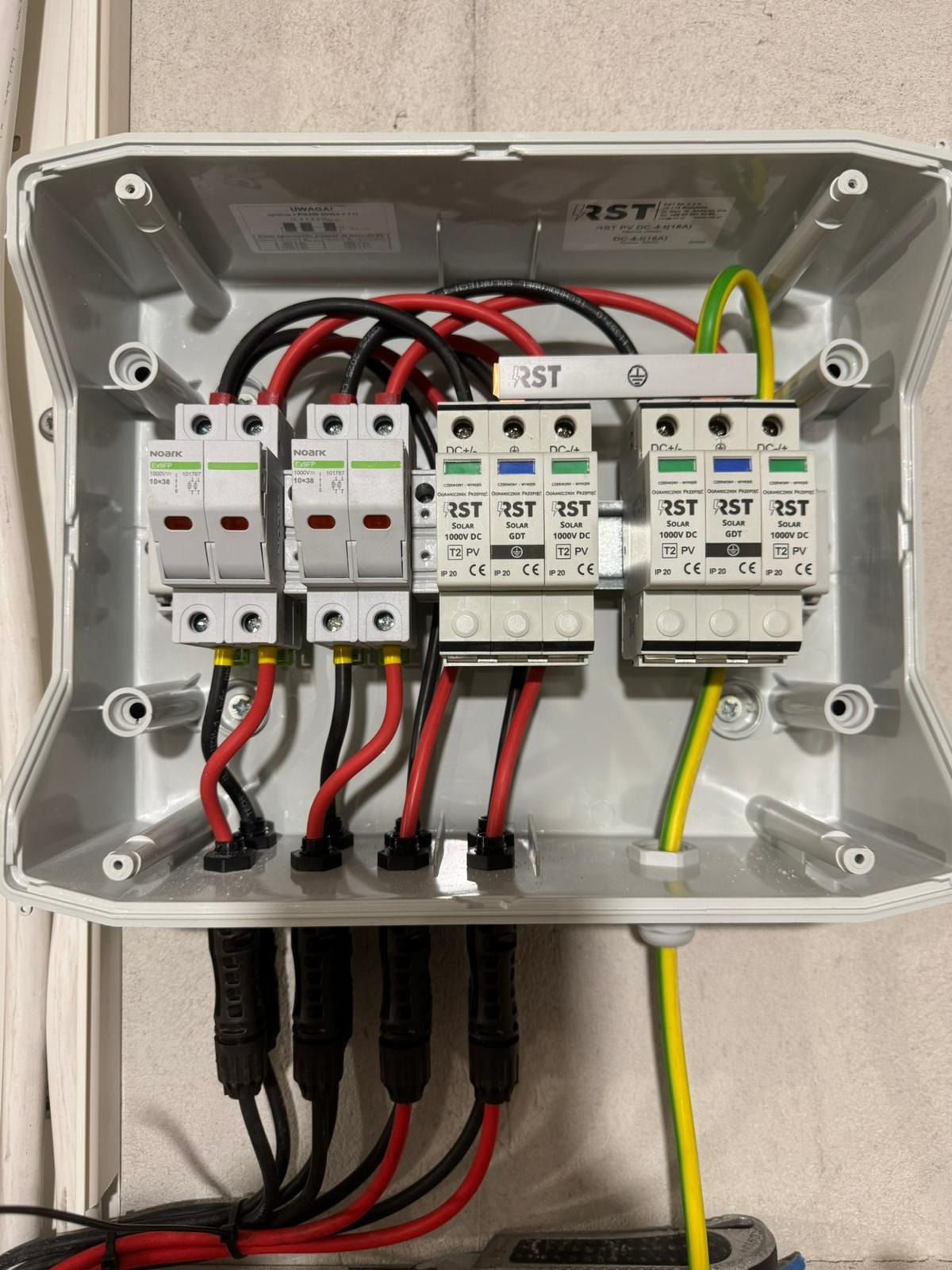 Rozdzielnica DC z bezpiecznikami Noark i ogranicznikami przepięć RST, okablowana czerwonymi i czarnymi przewodami, żółto-zielony przewód uziemiający.