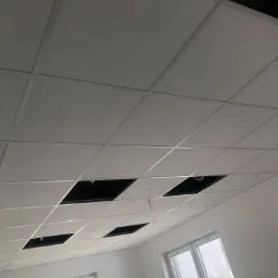 Sufit podwieszany z płyt kartonowo-gipsowych w trakcie montażu, widoczne otwory na instalacje, okna w tle.