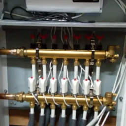 Rozdzielacz ogrzewania podłogowego z zamontowanymi siłownikami termoelektrycznymi i sterownikiem TECH w szafce instalacyjnej.