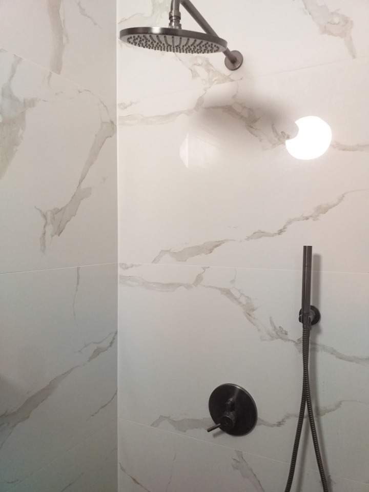 Nowoczesna kabina prysznicowa z deszczownicą i baterią w kolorze grafitowym, wykończona białymi płytkami imitującymi marmur.