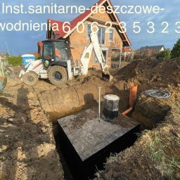 Usługi Koparko - Ładowarką Ponicki Radosław - Wykop pod zbiornik betonowy na działce z koparką JCB w tle. Widoczne rury kanalizacyjne i instalacje. Na górze zdjęcia numer telefonu.