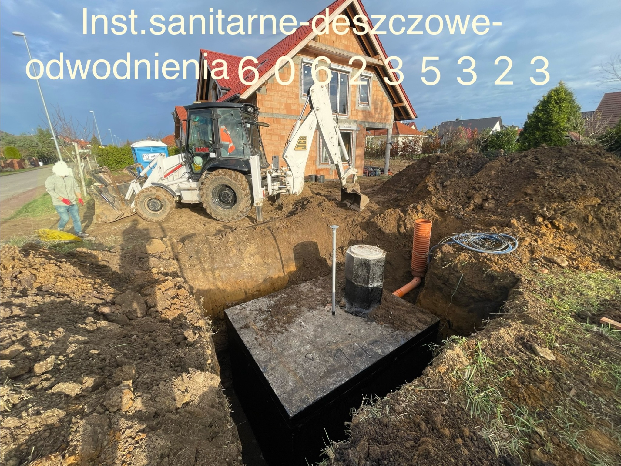 Wykop pod zbiornik betonowy na działce z koparką JCB w tle. Widoczne rury kanalizacyjne i instalacje. Na górze zdjęcia numer telefonu.