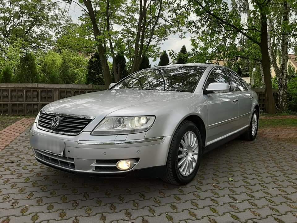 Srebrny Volkswagen Phaeton zaparkowany na brukowanym podjeździe, z widocznymi detalami chromowanymi i oświetleniem dziennym.