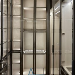 Nowoczesna garderoba z podświetleniem LED i szklanymi frontami, zaprojektowana w Chrzanowie. Minimalistyczny design, widoczne półki i wieszaki na ubrania.