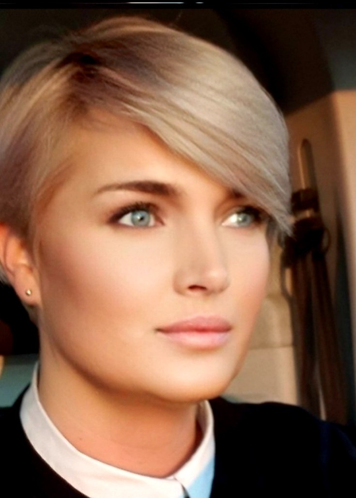 Portret kobiety o krótkich blond włosach, błękitnych oczach i delikatnym makijażu, ubrana w białą koszulę i ciemną marynarkę, spoglądająca w dal.