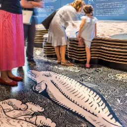 Dekoracyjna posadzka żywiczna z motywem mapy i morskich stworzeń w Sadowej, oglądana przez zwiedzających w muzeum.