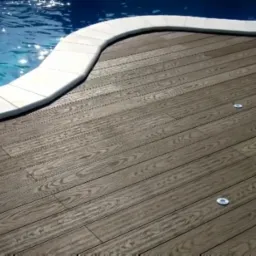 Drewniany taras z oświetleniem punktowym przylegający do basenu z białym obramowaniem.