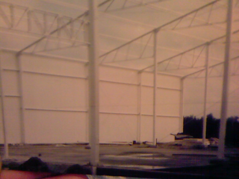 Wnętrze nowo budowanego, dużego magazynu z metalową konstrukcją szkieletową pomalowaną na biało i betonową posadzką w trakcie wylewania.